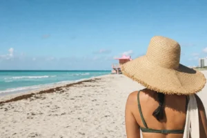Eine Frau mit Strohhut blickt auf einen türkisfarbenen Strand